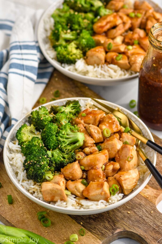 Overhead photo of two plates of teriyaki chicken bowl served with broccoli over rice and two forks for eating.