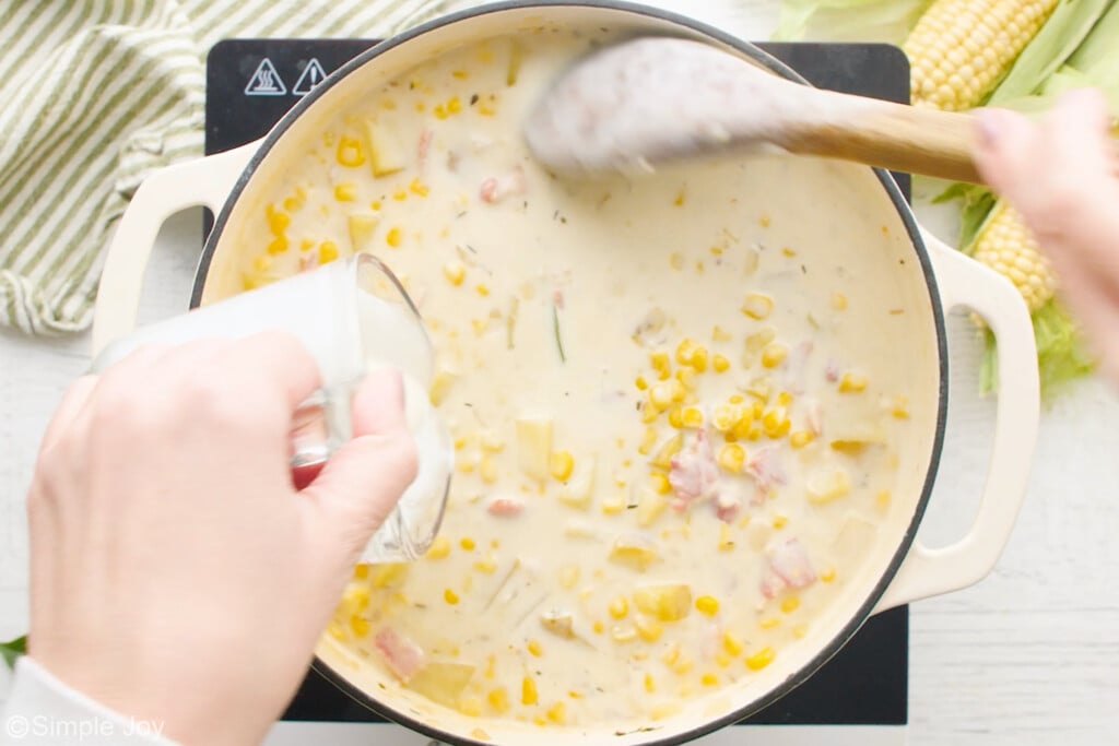 pouring cream from a measuring cup into corn chowder and stirring it in with a wooden spoon