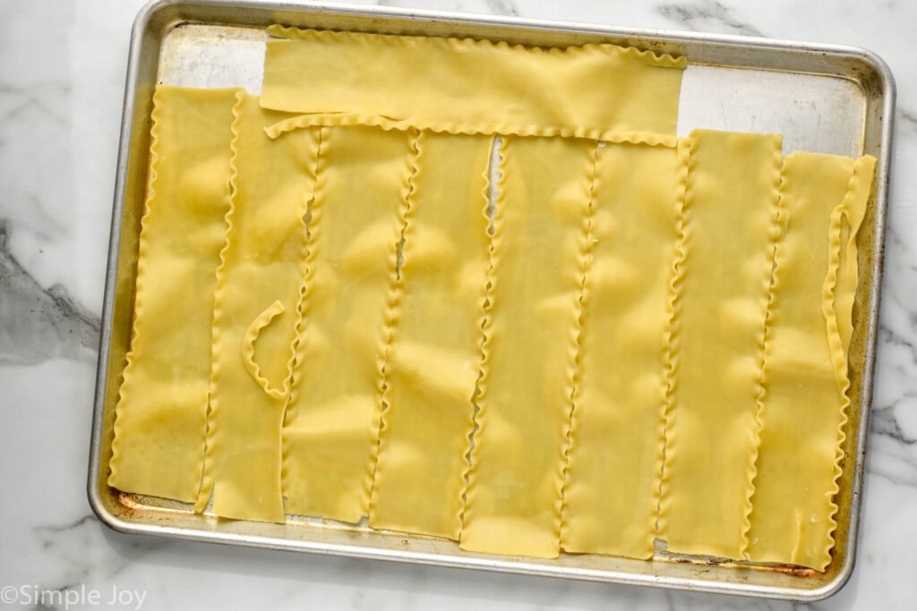 overhead of a rimmed baking sheet with a single layer of cooked lasagna sheets