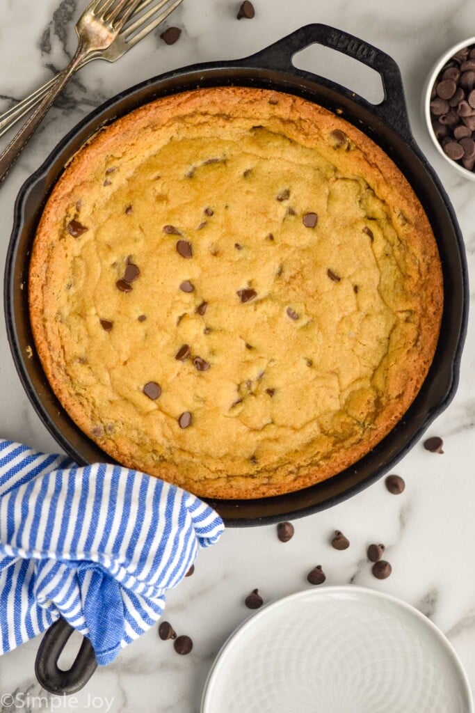 Overhead photo of Pizookie recipe in a skillet. Chocolate chips and forks sit on counter beside skillet.