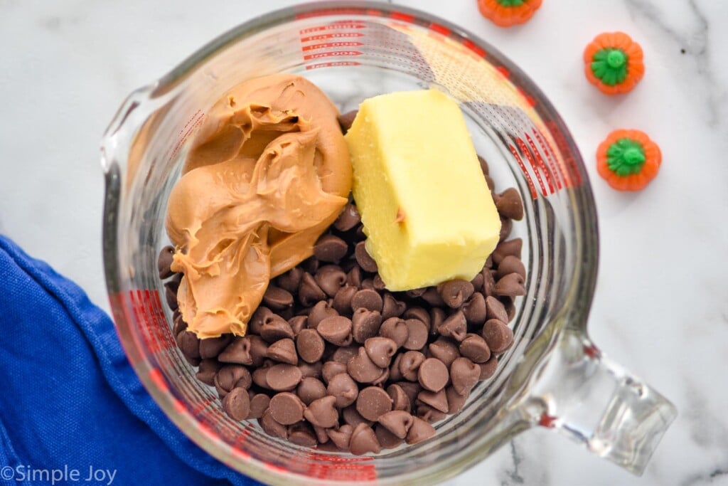 Overhead photo of butter, peanut butter, and chocolate chips in a glass measuring cup for Pumpkin Spice Muddy Buddies.