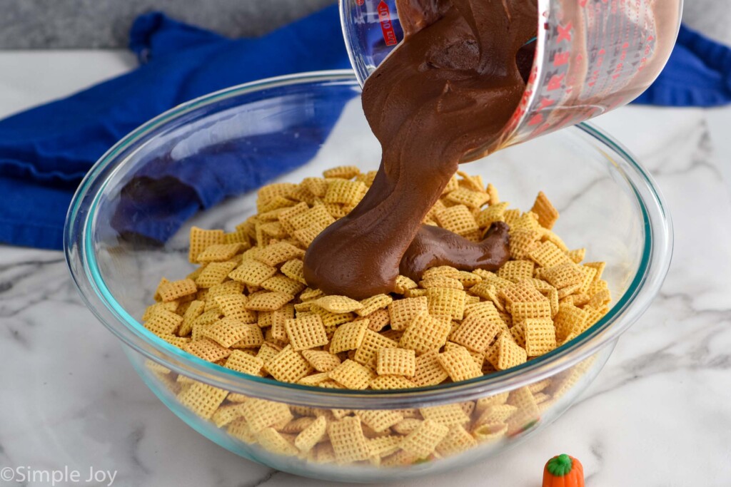 Overhead photo of melted chocolate mixture being poured over bowl of Chex cereal for Pumpkin Spice Muddy Buddies recipe.