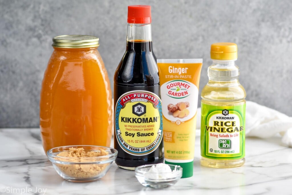 Photo of Teriyaki Sauce recipe ingredients including a jar of honey, a glass cup of brown sugar, a bottle of soy sauce, a tube of ginger paste, a bottle of rice vinegar, and a glass dish of corn starch.
