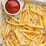 Pinterest graphic for Easy French Fries recipe. Text says, "Easy Baked truly crispy french fries simplejoy.com." Image is overhead photo of easy french fries on a baking sheet with a dish of ketchup for dipping.