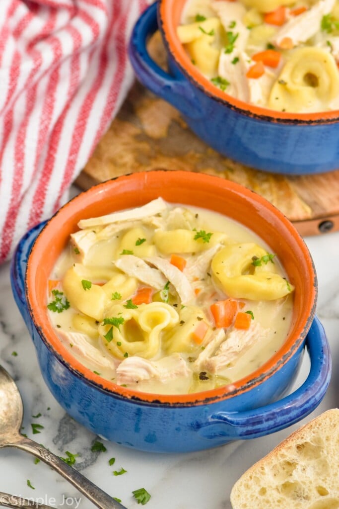 overhead view of two bowls of chicken tortellini soup with spoon and piece of bread laying beside