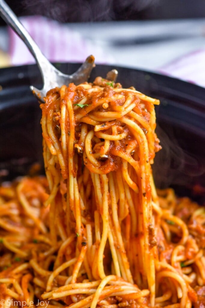 Close up photo of crock pot spaghetti recipe. A fork is pulling a portion out from the slow cooker.