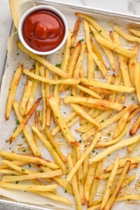 Overhead photo of Easy French Fries on a baking sheet with a dish of ketchup for dipping.