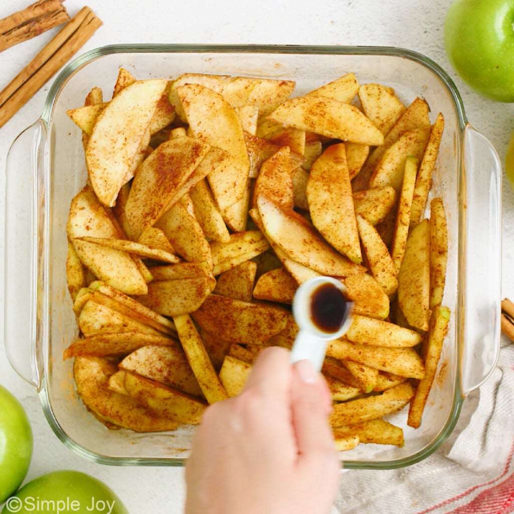 overhead of vanilla extract being poured over cut apples tossed in cinnamon