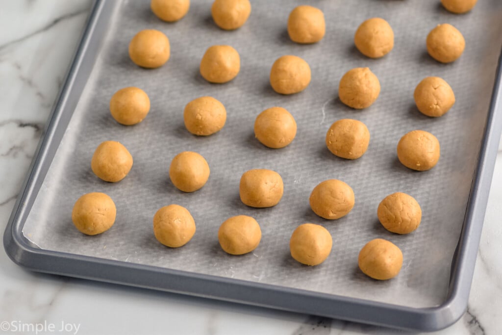 Overhead photo of Peanut Butter Balls recipe in the process. Peanut butter balls are laid out on a parchment paper-lined baking sheet.