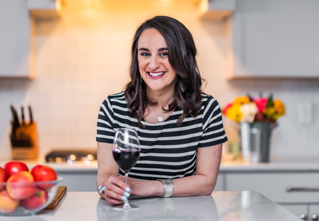 a woman leaning into a counter with her hand on the stem of a wine glass