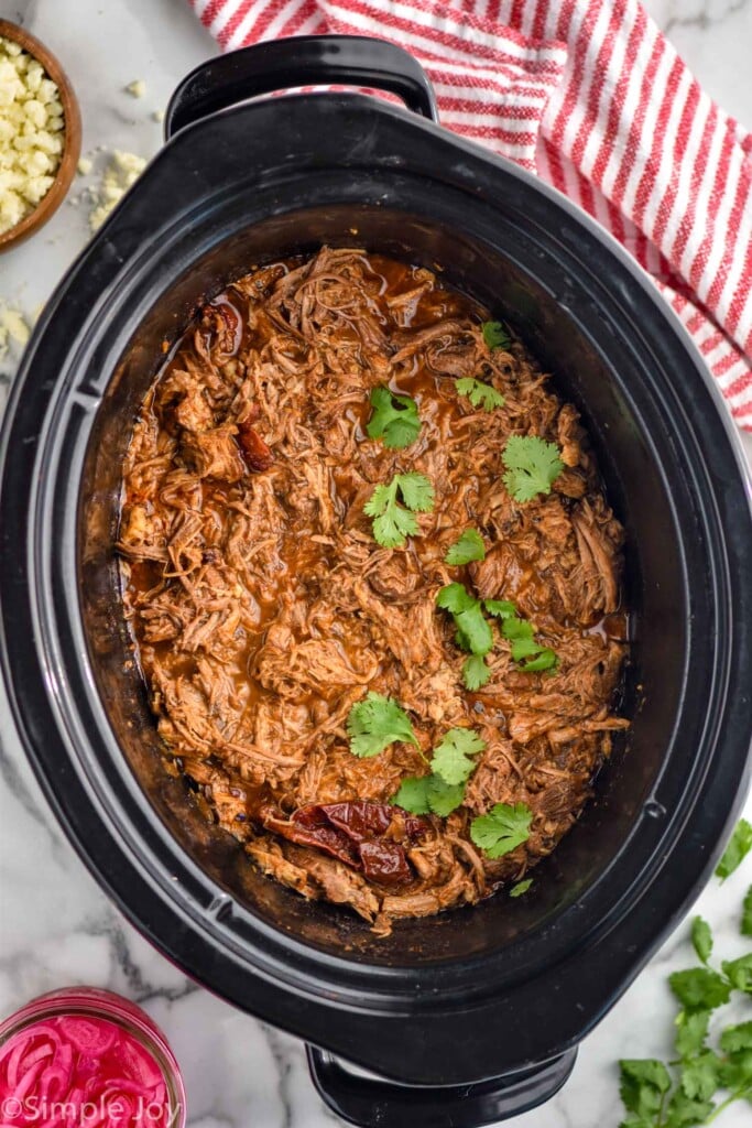 Overhead photo of pork in a crock pot for pulled pork tacos recipe. Garnished with cilantro.