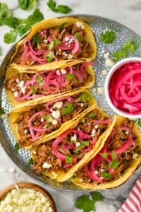 Overhead photo of Pulled Pork Tacos served with pickled red onion and garnished with cilantro.