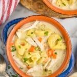overhead view of two bowls of chicken tortellini soup with spoon and piece of bread laying beside - 9
