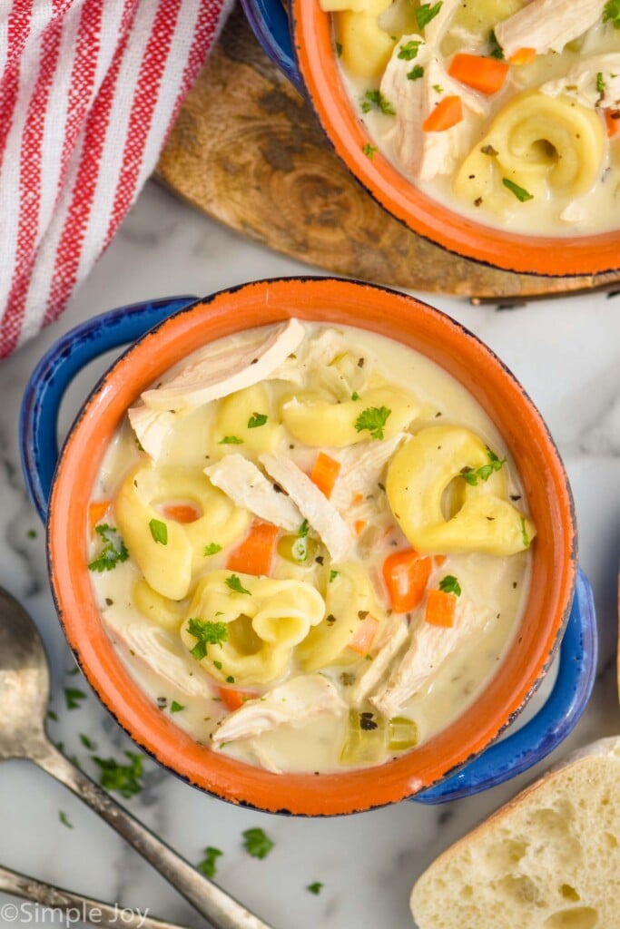 overhead view of two bowls of chicken tortellini soup with spoon and piece of bread laying beside