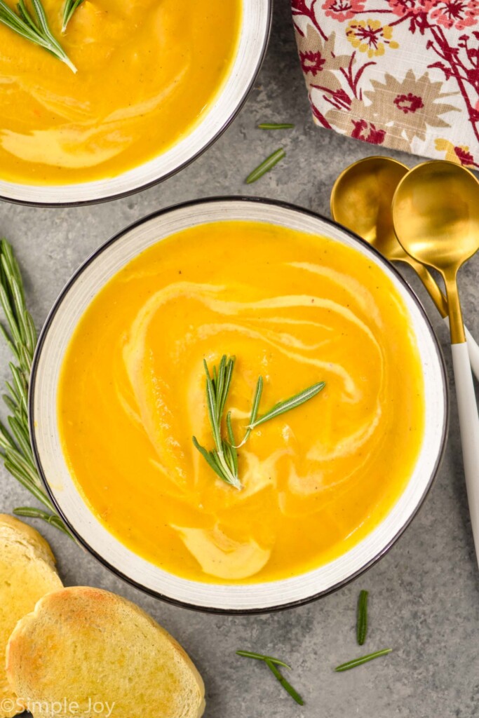 Overhead photo of a bowl of Acorn Squash Soup with bread and spoons for eating.