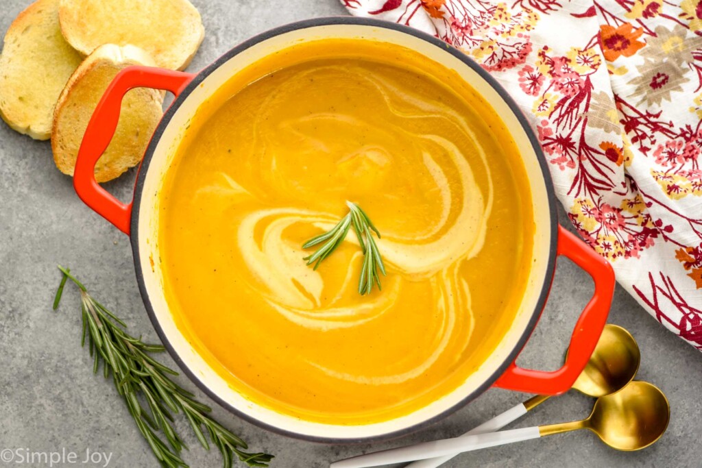 Overhead photo of Acorn Squash Soup in a pot. Bread and spoons are beside pot on counter.