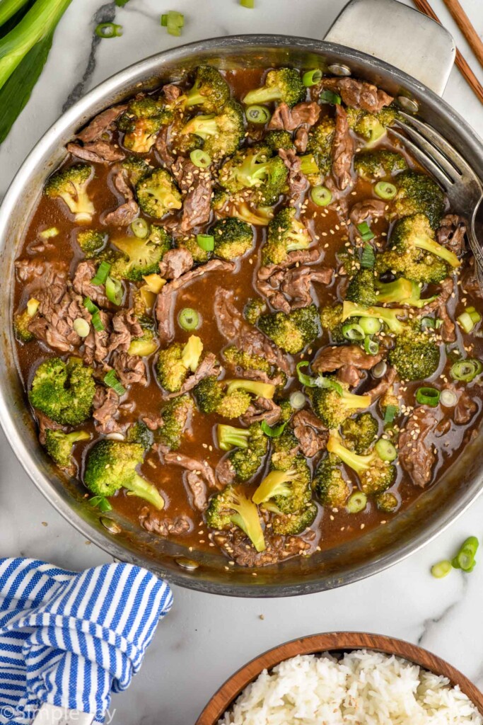 overhead of pan of beef teriyaki with broccoli. Bowl of rice sitting in background for serving.