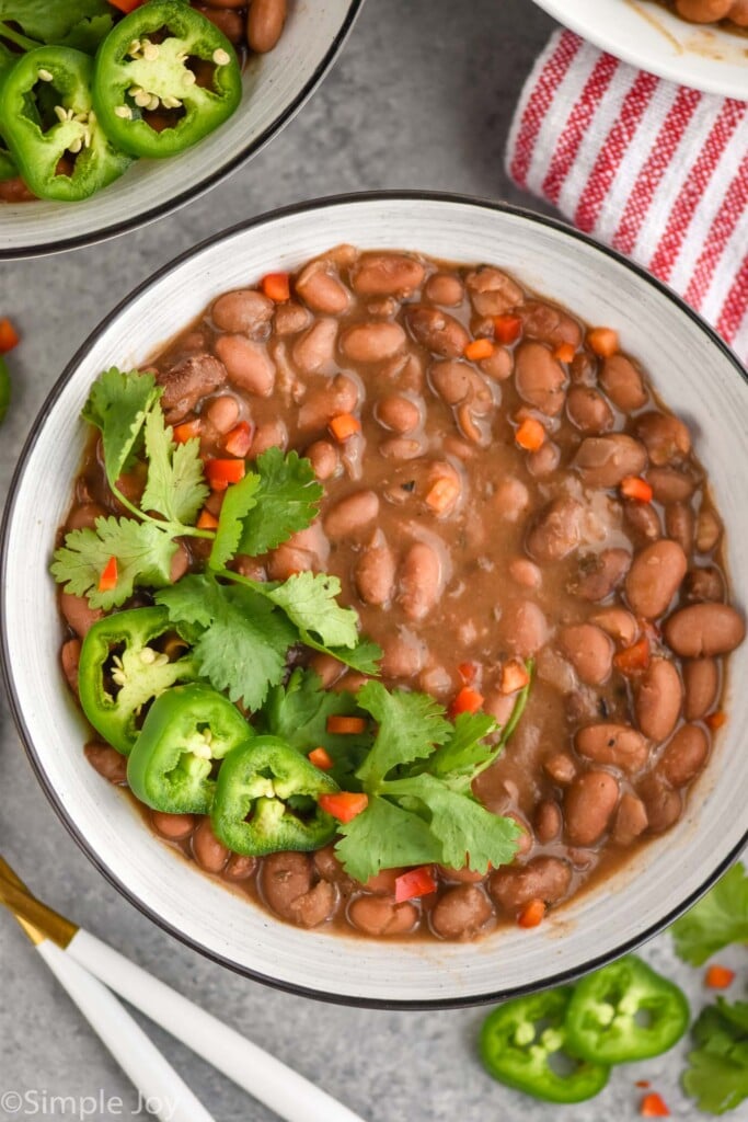 overhead of crock pot pinto beans in a bowl, garnished with jalapeños and cilantro 