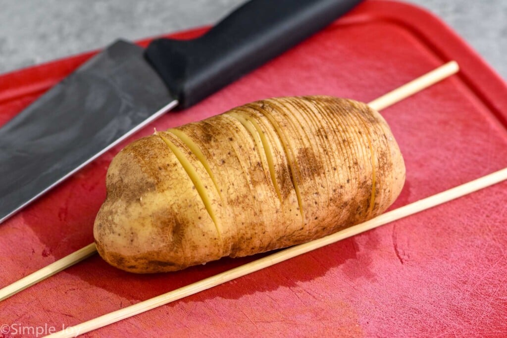 potato sliced for hasselback potatoes on cutting board with wooden skewers and knife laying beside