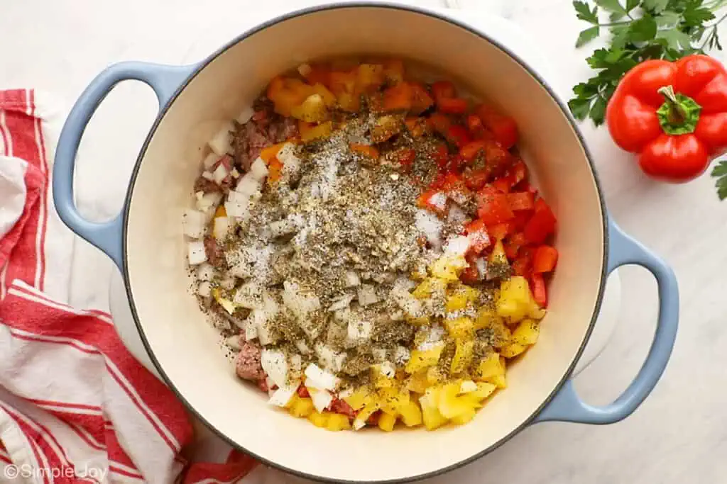 overhead of a stock pot with ground beef, chopped peppers, and onions