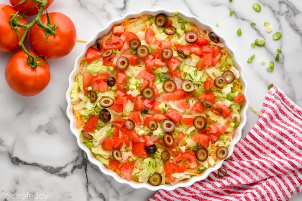 Overhead photo of Taco Dip. Tomatoes sit on counter beside taco dip.