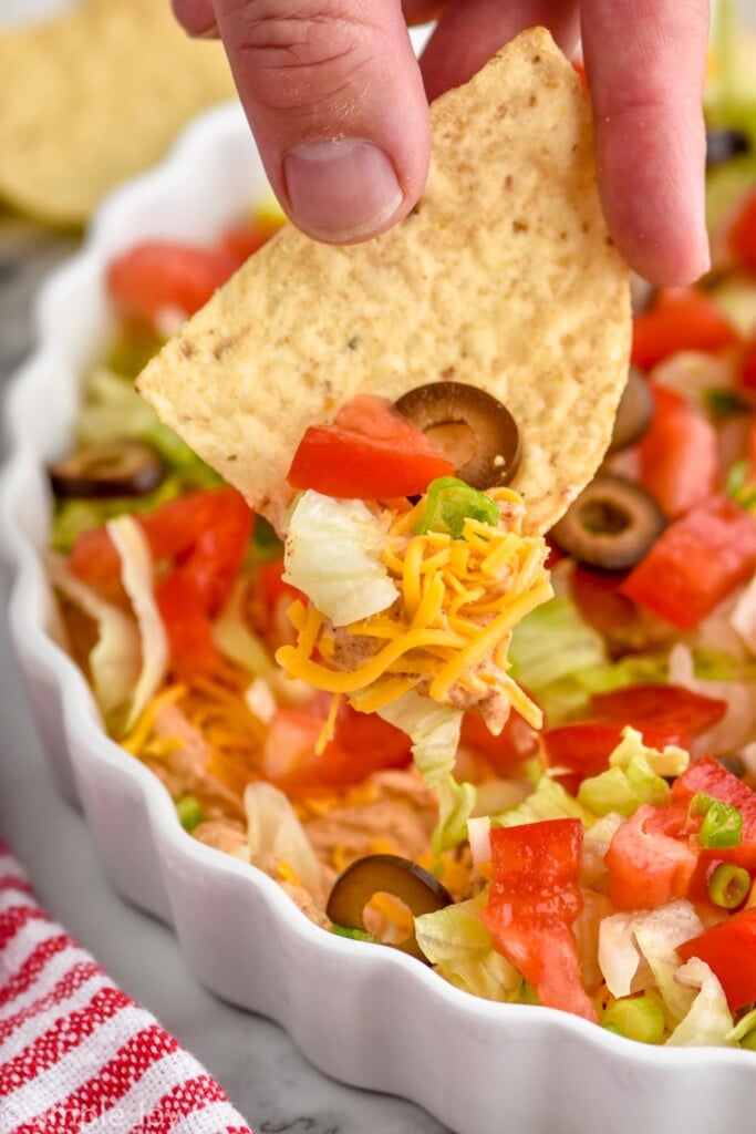 Overhead photo of man's hand scooping a tortilla chip into Taco Dip recipe.