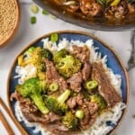 overhead of a bowl of beef teriyaki with broccoli served over rice. Pan of beer teriyaki recipe sitting beside.