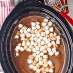 Pinterest photo of overhead of crockpot hot chocolate in a 6 quart crockpot with mini marshmallows in it and cocoa powder and chocolate chips in the background, says slow cooker hot chocolate