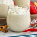 Pinterest graphic of homemade eggnog with whipped cream in a stemless wine glass with cinnamon sticks and bottle of eggnog in the background says homemade eggnog simple joy.com