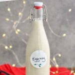 Bottle of homemade eggnog with a red towel and sparkling lights in the background