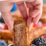 Pinterest graphic for French Toast Sticks. Text says "homemade french toast sticks simplejoy.com" Image shows man's hand dipping french toast stick into syrup with plate of french toast sticks and fresh berries sitting behind.