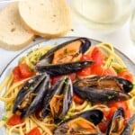 Pinterest graphic for mussels recipe. Image shows plate of pasta with tomatoes and mussels. Text says "the best mussels recipe simplejoy.com"