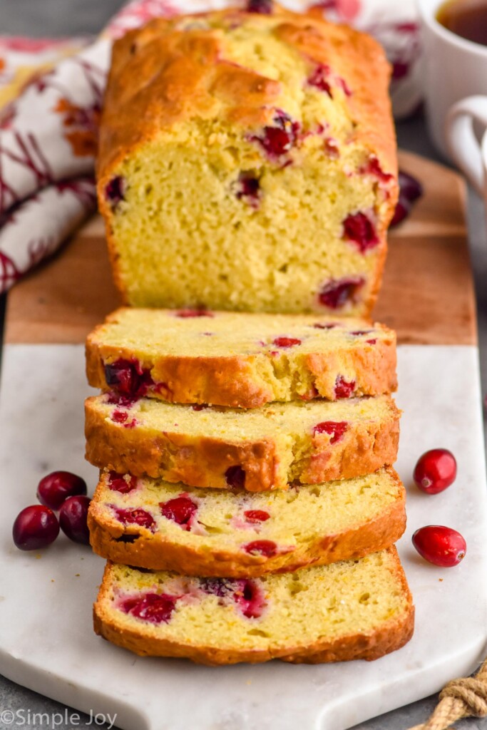 sliced loaf of orange cranberry bread on a cutting board with cranberries sitting beside.