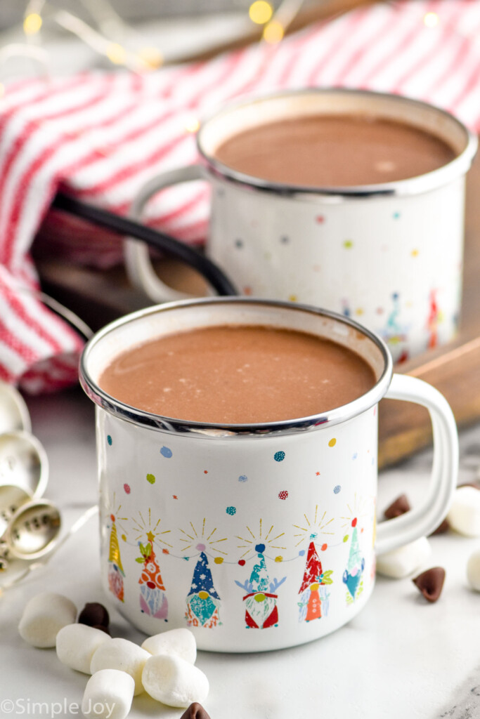 Overhead photo of two Crockpot Hot Chocolates in festive mugs with marshmallows surrounding the mugs