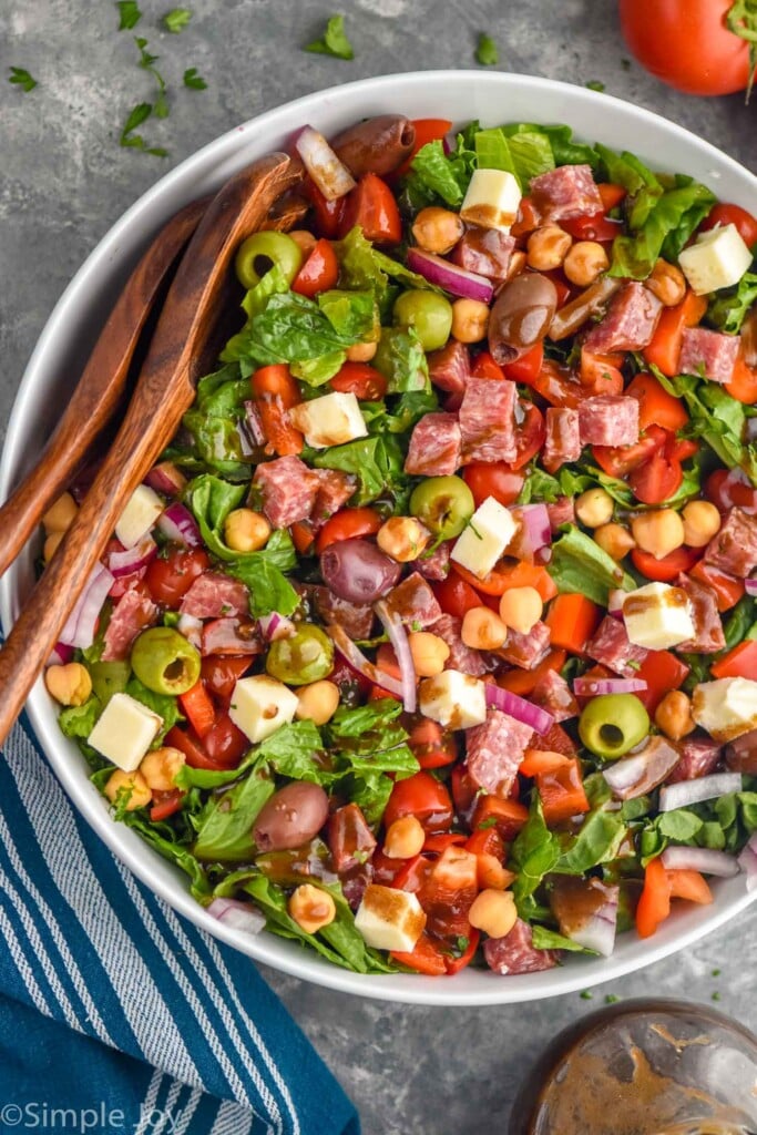 overhead photo of a chopped salad in a white bowl with wooden serving spoons