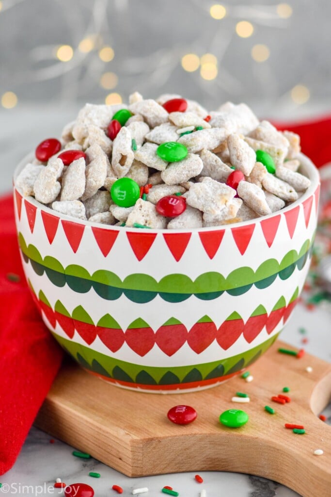 bowl of Christmas Puppy Chow with sprinkles and chocolate candies surrounding
