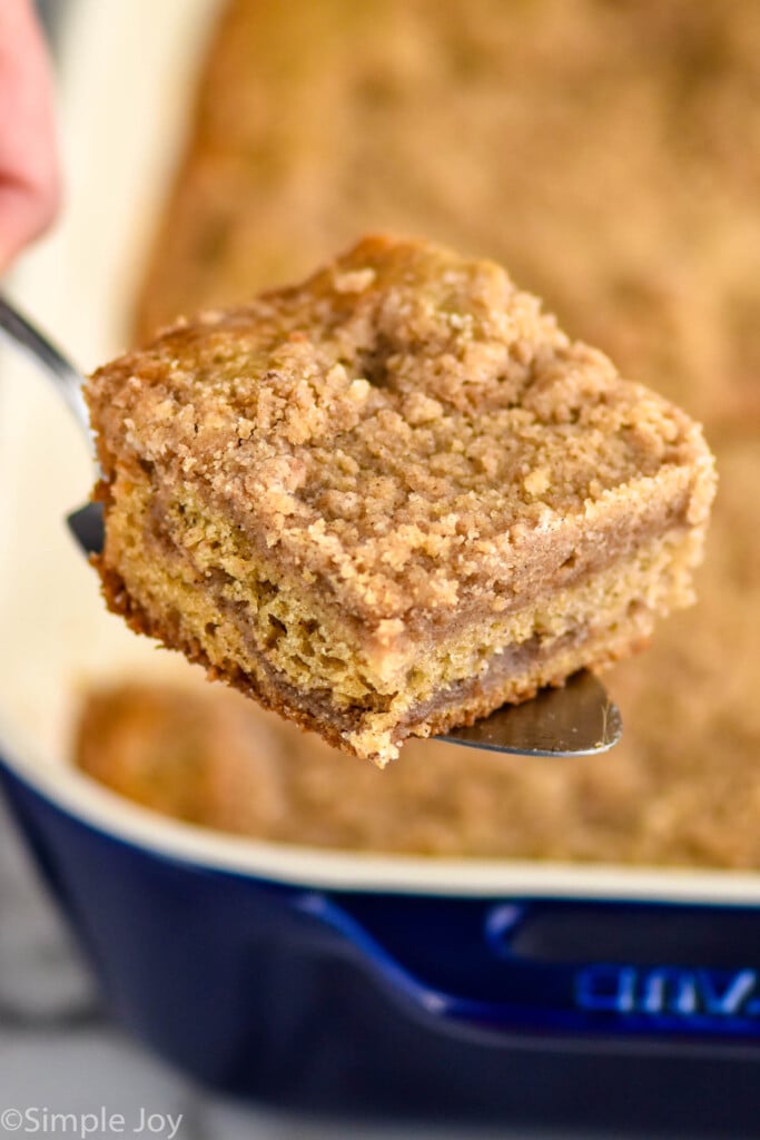 Serving spatula holding piece of coffee cake with pan of coffee cake sitting in background