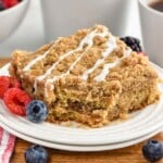 piece of coffee cake on a plate with fresh fruit. Mugs of coffee sitting in background - 9