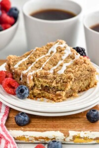 piece of coffee cake on a plate with fresh fruit. Mugs of coffee sitting in background