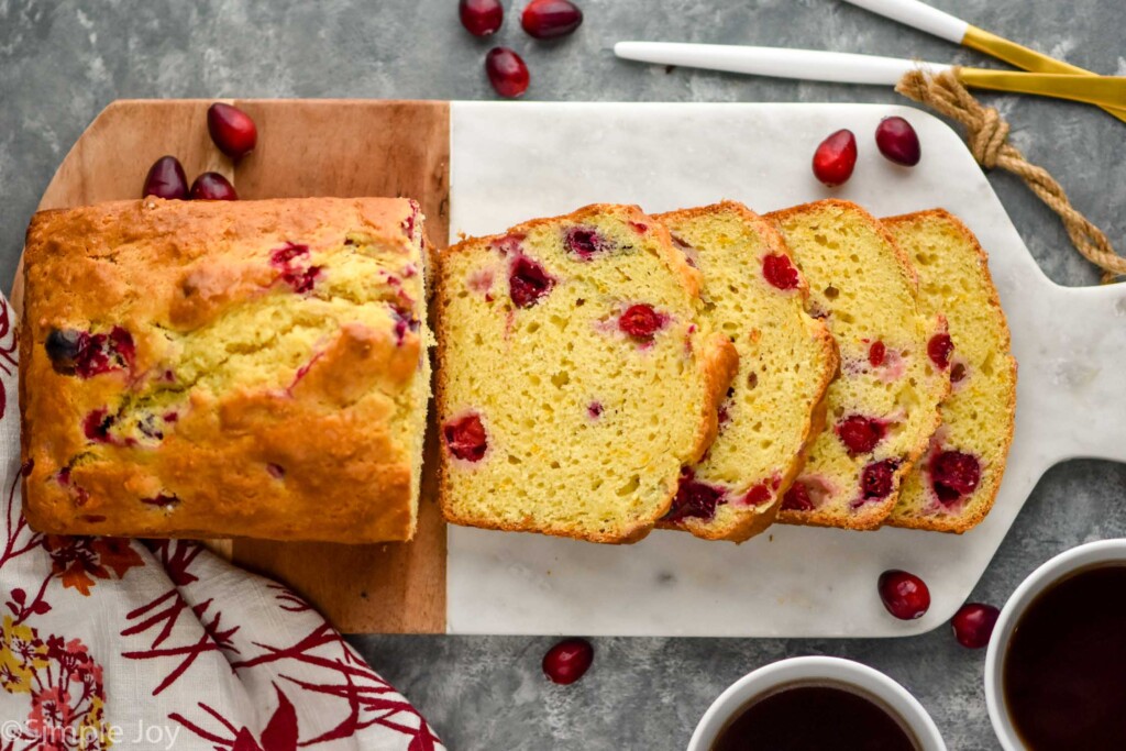 overhead of sliced loaf of orange cranberry bread on a cutting board with cranberries sitting beside.
