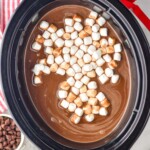 Overhead photo of crockpot hot chocolate in a 6 quart crockpot with mini marshmallows in it and cocoa powder and chocolate chips in the background - 8