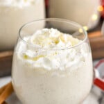 Overhead photo of homemade eggnog with whipped cream in a stemless wine glass with sparkling lights in background