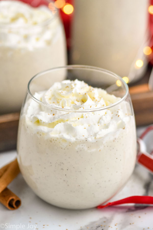 Overhead photo of homemade eggnog with whipped cream in a stemless wine glass with sparkling lights in background