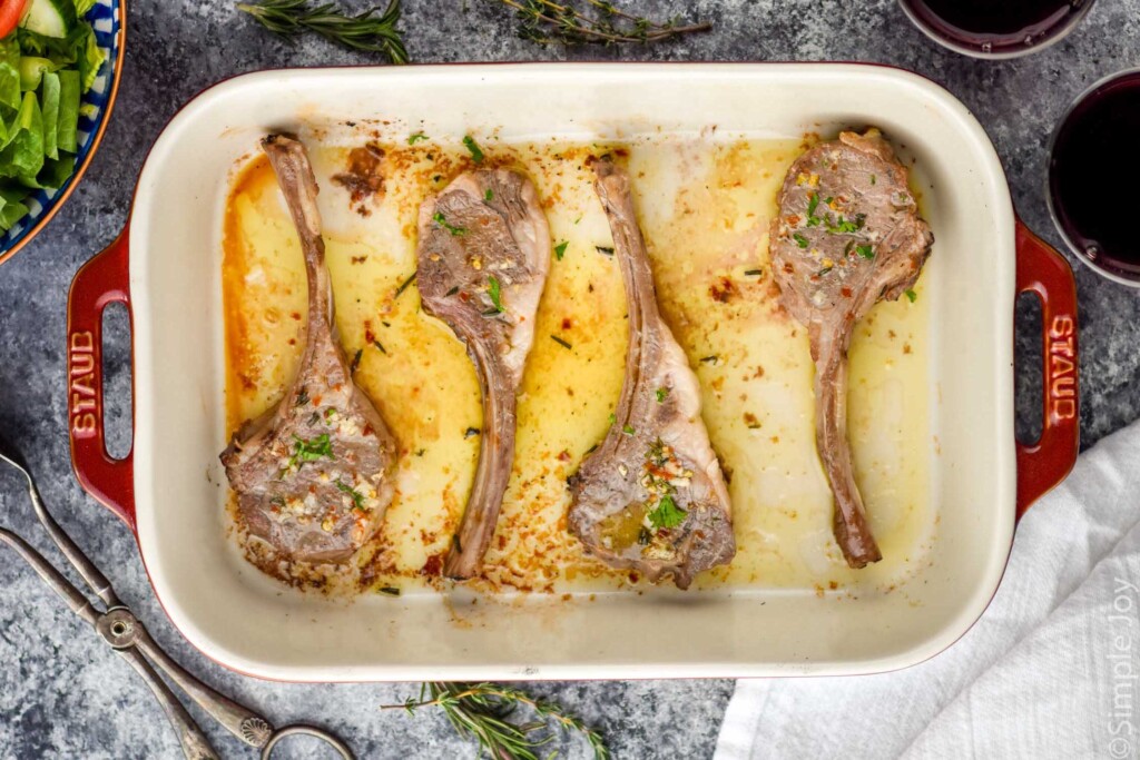 Overhead photo of four easy lamb chops in a white baking pan