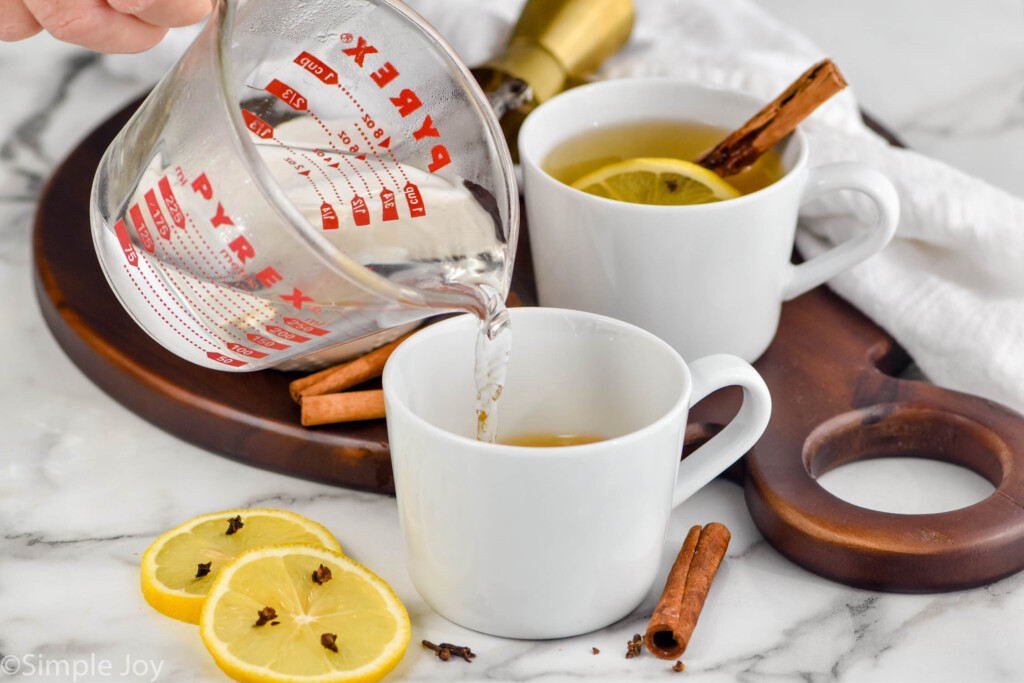 How to make a hot toddy image of hot water being poured into a white mug with a lemon slice and a Hot Toddy in the background