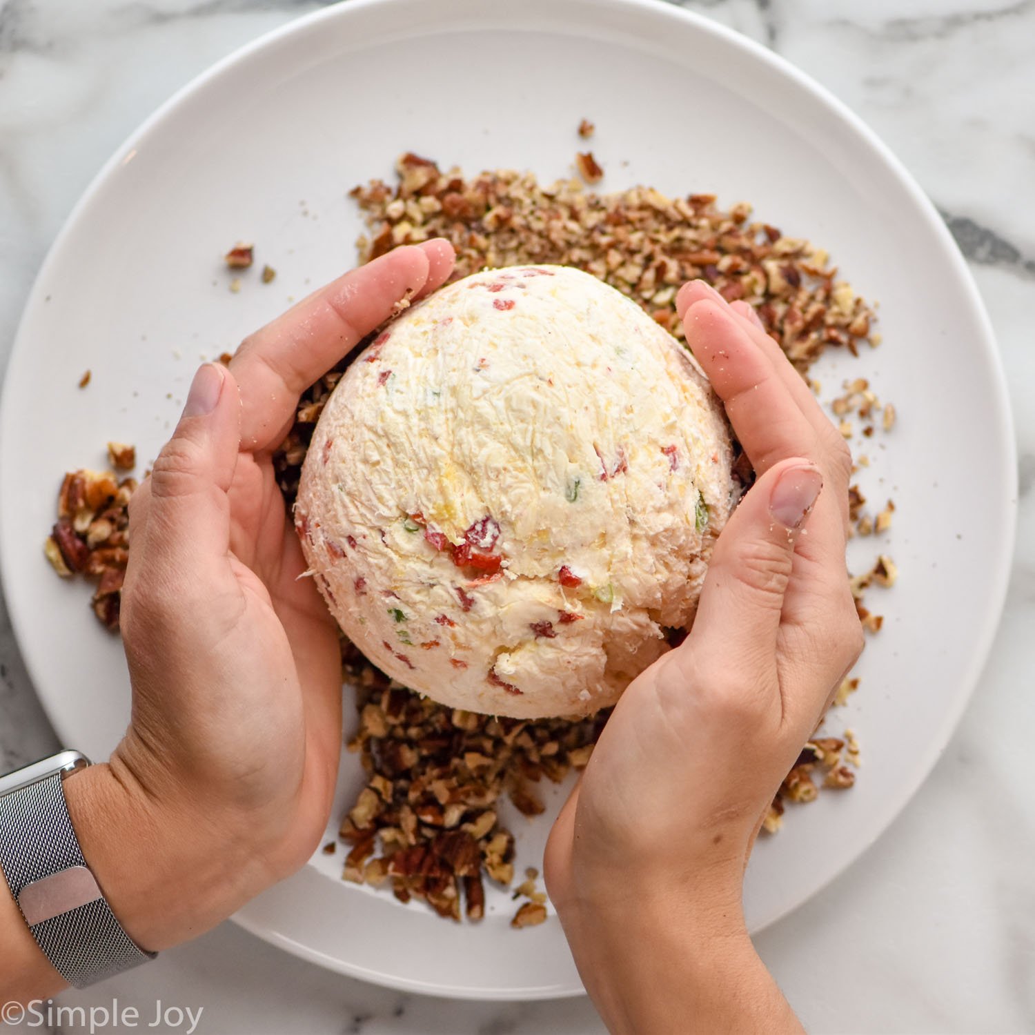 women's hands coating pineapple cheese ball in pecans