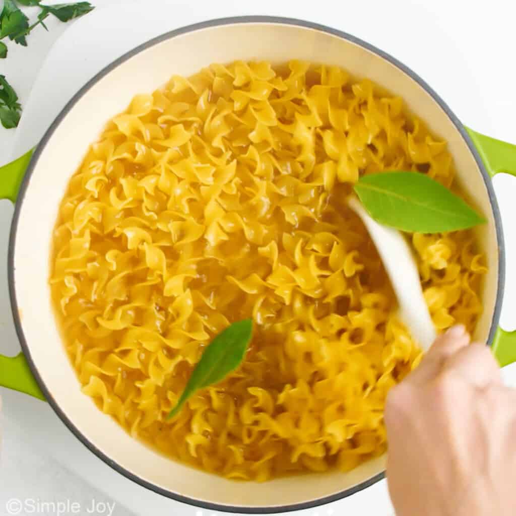 overhead of a pot of egg noodles boiling with bay leaves