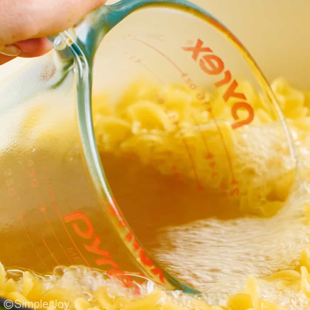 a measuring cup scooping up broth egg noodles have been boiled in