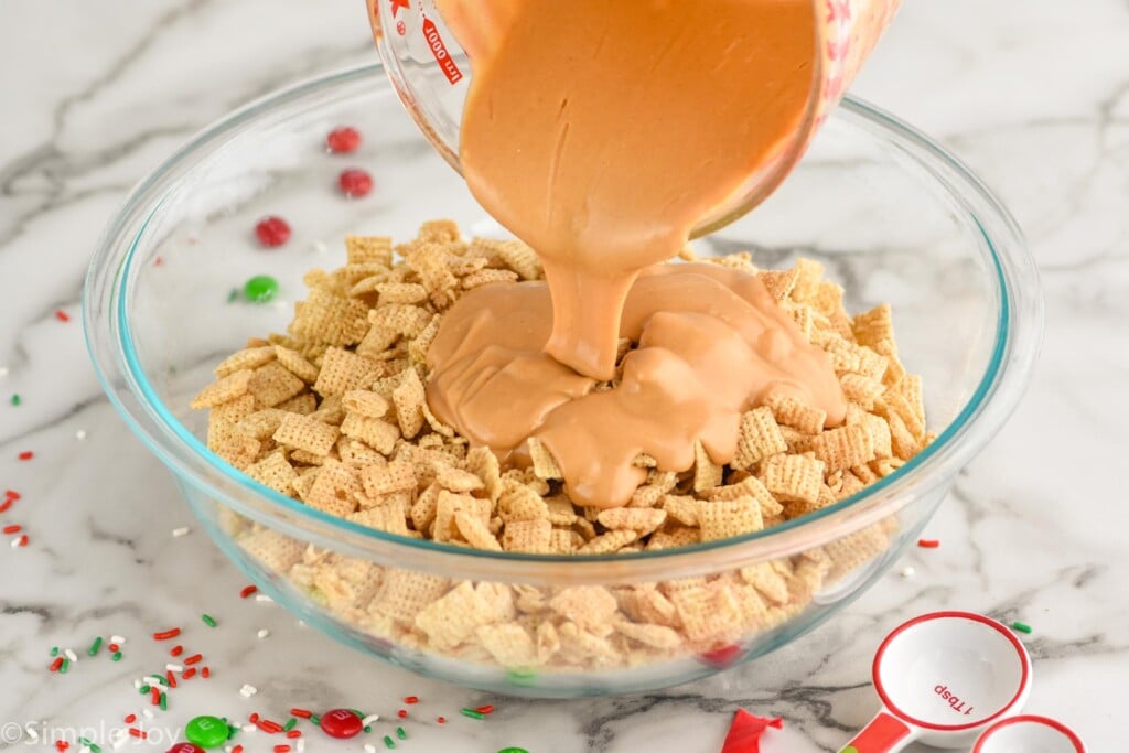 glass measuring cup pouring melted Christmas puppy chow ingredients into a bowl of chex cereal to make Christmas Puppy Chow.