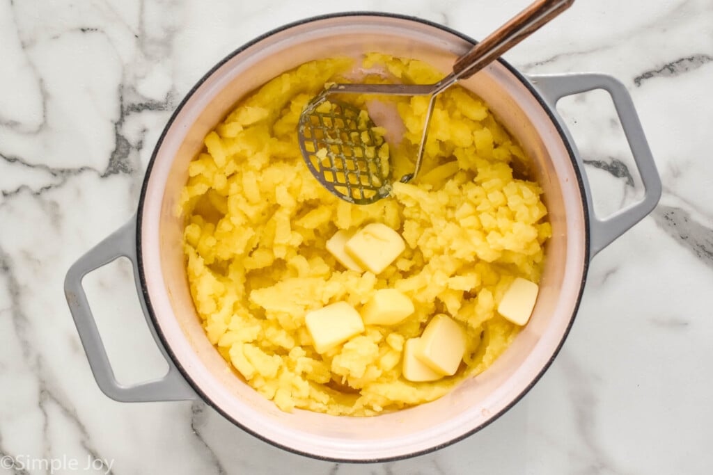 overhead pot of potatoes with butter and potato masher on top to make mashed potatoes